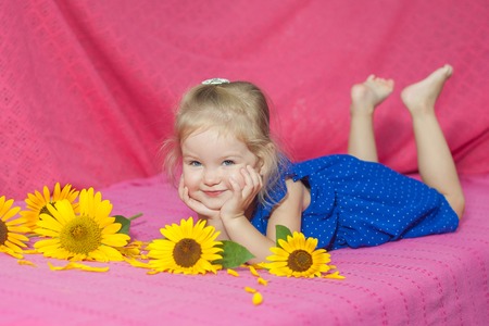 The child with with apples and sunflowers lying on pink blanket at homeの写真素材