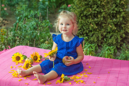 The child with with apples and sunflowers sitting on pink blanket in gardenの写真素材