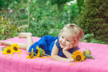 The child with with apples and sunflowers lying on pink blanket in gardenの写真素材