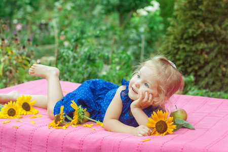 The child with with apples and sunflowers lying on pink blanket in gardenの写真素材