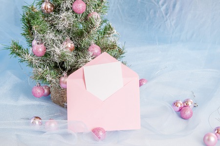 Christmas Holiday Background, Hanging pink baubles on Christmas tree, New Year backdrop, Decoration. Abstract blue Blurred Bokeh. Christmas Tree decorated. pink open envelope with paper, greeting cardの写真素材