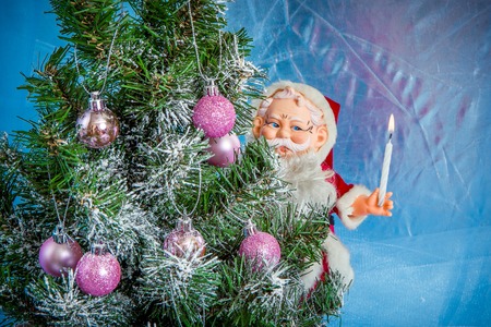 Christmas Holiday Background, Hanging pink baubles on Christmas tree, New Year backdrop, Decoration. Christmas Tree decorated. Toy Santa Claus with burning candleの写真素材