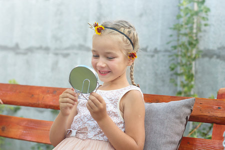 Little girl looks in the mirror, paints lips with lipstick, admires her reflection. Happy, Cute, funny.の写真素材