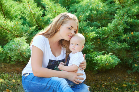 Happy beautiful mother and baby daughter or son enjoying in the summer parkの写真素材