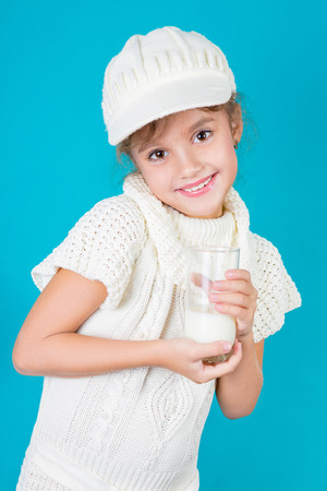 Beautiful little girl drinking fresh milk, on a blue backgroundの写真素材