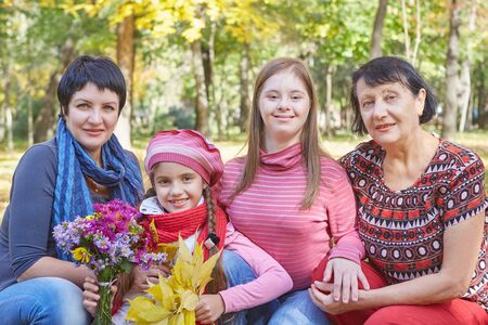 Happy family. Loving mother, Grandmother and two daughter in autumn park. One daughter with a disability with Down syndrome. Positive human emotions, feelings.の写真素材