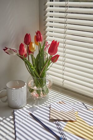 Spring still life scene. Cup of coffee, opened notebook,  on windowsill.  Floral composition with tulips.の写真素材