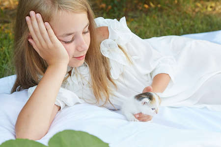 Little girl lying in bed in summer garden with kittenの写真素材