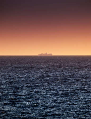 A freight ship sailing on the horizon during a summer sunsetの写真素材