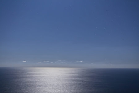 Night time exposure showing a clear sky and the ocean washed in the light of the full moon.の写真素材