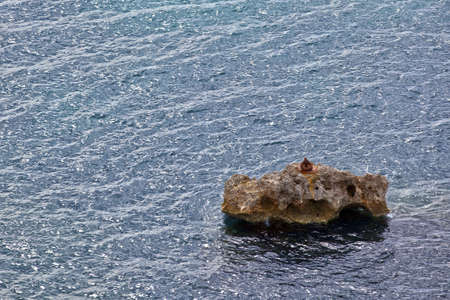Jagged rock out at sea with textured ocean surface backdropの写真素材