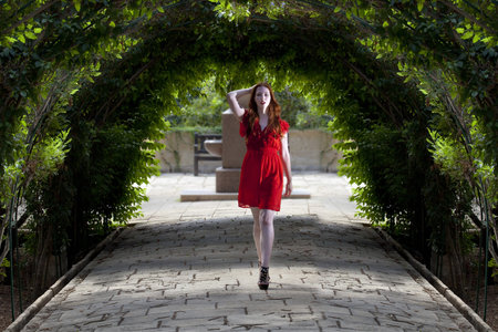 Young woman in red dress walking under arches of foliageの写真素材