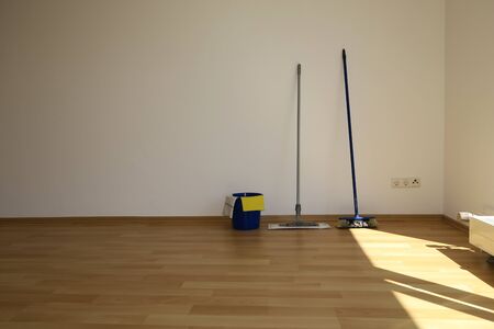 A mop and bucket and a room standing on a parquet floor in front of a white wall.の写真素材