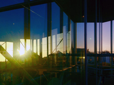 The sunset is reflected in the glass facade of a building over the rooftops of Amsterdam. In the background is an urban silhouette and the purple-colored sky.の写真素材