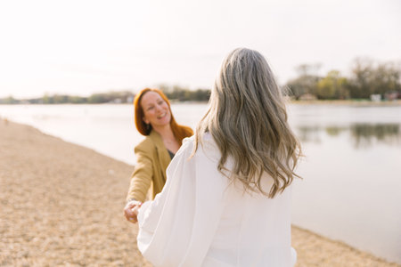 An adult daughter with a gray-haired mother on a walk on the beach, laughing and smiling. Happy old age and care for the elderlyの写真素材