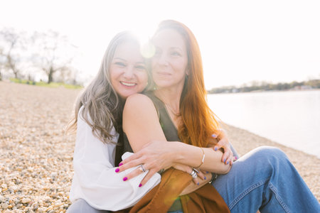 An elderly gray-haired mother and her adult daughter sit on the shore and cuddle. Caring for an elderly mother and the concept of a happy retirement and old age. close upの写真素材
