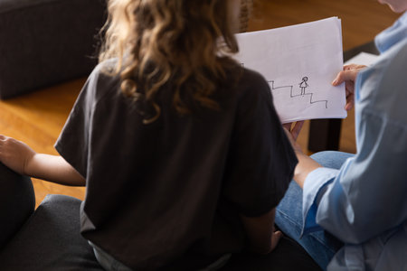 A girl at a psychologists appointment draws a test drawing, low self-esteem and psychological problems in a child, a photo from the backの写真素材