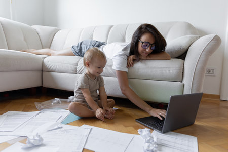 Young girl sitting on the couch and trying to work next to the child. Procrastination and deadline at workの写真素材