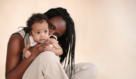 African-American mother with baby on beige background Minimalist portraits, space for textの写真素材