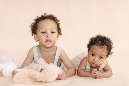 African-American children, a baby girl and a 4-year-old boy looking at the camera on a beige background, a minimalist portrait.の写真素材