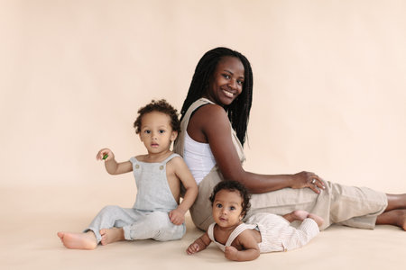 happy African-American baby and child with mother on a beige background in the style of minimalismの写真素材