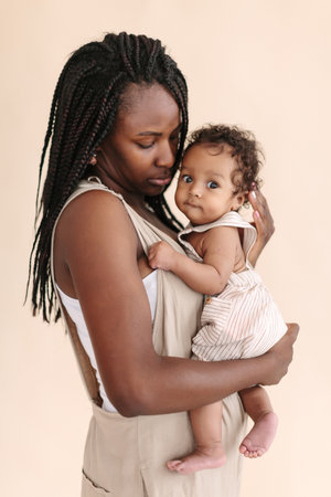 African-American mother with baby smiles and rejoices on beige background Minimalist portraits, space for textの写真素材
