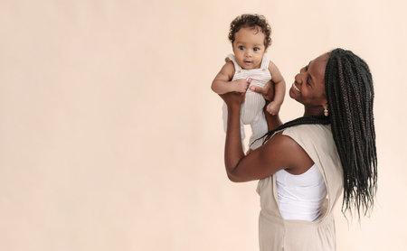 African-American mother with baby smiles and rejoices on beige background Minimalist portraits, space for textの写真素材