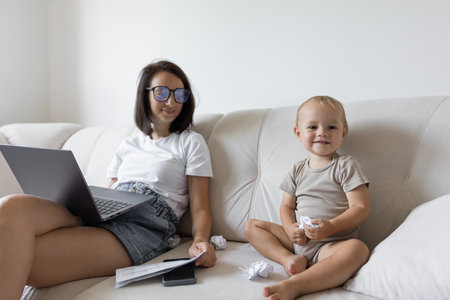 Young girl sitting on the couch and trying to work next to the child. Procrastination and deadline at workの写真素材