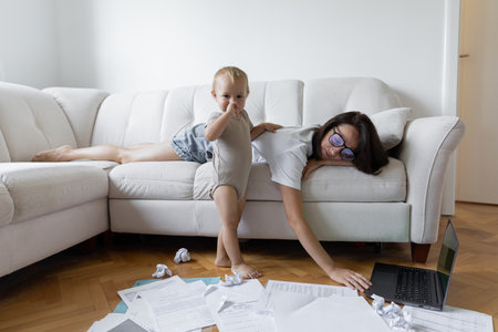 Young girl sitting on the couch and trying to work next to the child. Procrastination and deadline at workの写真素材