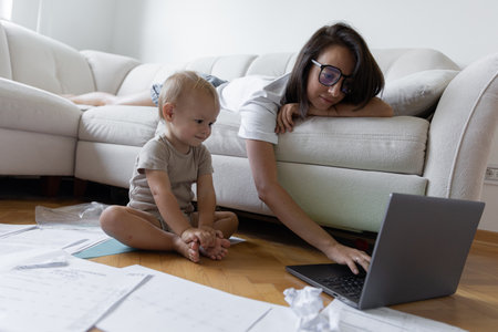 Young girl sitting on the couch and trying to work next to the child. Procrastination and deadline at workの写真素材