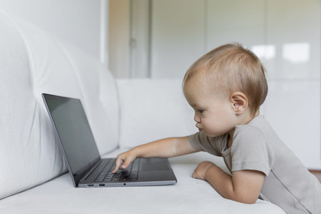 A little boy works on a laptop, presses buttons in a room at home. A small programmer, the concept of early development and online education.の写真素材