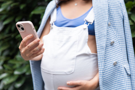 Pregnant girl using phone or app, close shot without faceの写真素材