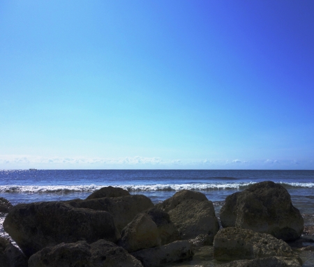 The stony coast, sea wave, the blue sky and the boat on the horizonの写真素材