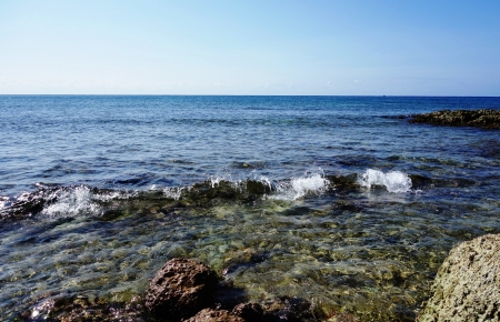 The stony coast, sea wave, the blue sky and the boat on the horizonの写真素材