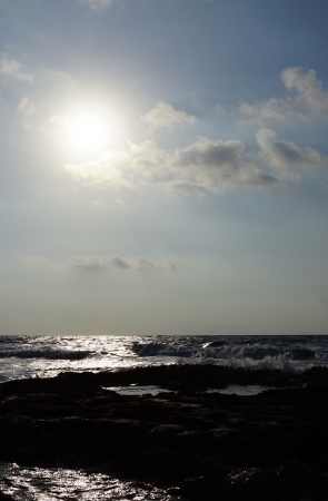 Morning sea surf on the stony coast, a rising sun among cloudsの写真素材