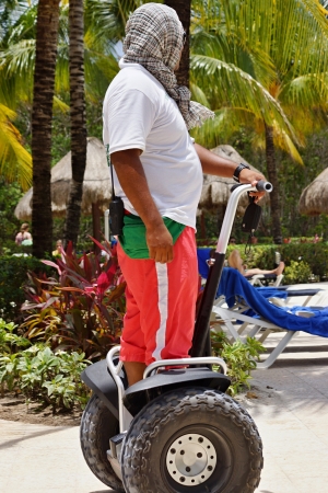 The man in a white t-shirt, in red trousers and in a scarf on the head riding segway on a beachのeditorial素材