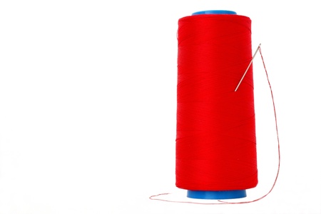 The sewing needle sticks out in the coil with red threads on a white backgroundの写真素材