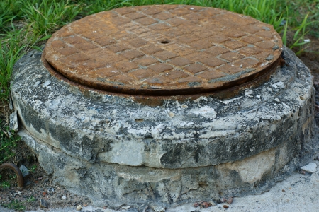 The old rusty pig-iron hatch for an entrance to a water waste collector of the sewerageの写真素材