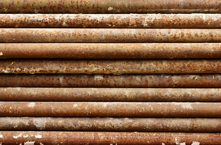 Old rusty iron pipes from construction scaffolds are laid in a stackの写真素材