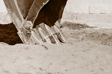 part of an old bucket with steel teeth for the excavator on a sand background of color sepiaの写真素材