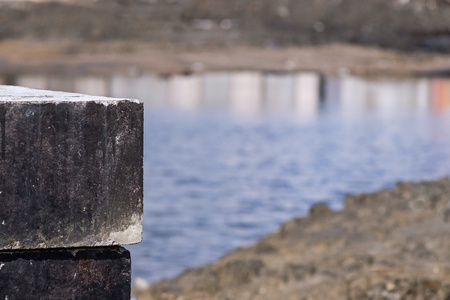 part of a design of concrete base black blocks on an indistinct background of gray coast and blue water with reflectionの写真素材