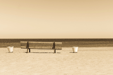 one wooden sepia bench and buckets on the sandy beach coast of the sea gulf and against the horizon of the sky and waterの写真素材