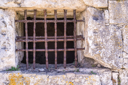 window lattice from old rusty iron on a stone wall of ancient dungeon or a prison