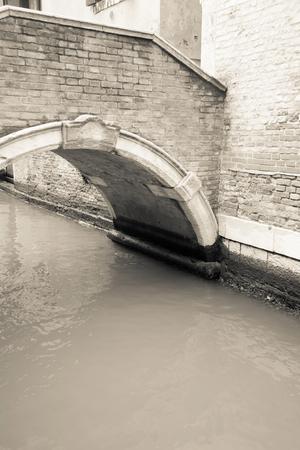 the old water channel with the brick arch bridge in ancient Italian Venice in retro styleの写真素材