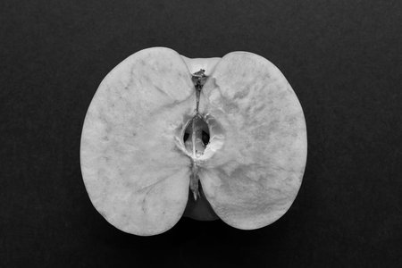 longitudinal cut or section of one apple as the isolated object closeup on black or against a dark backgroundの写真素材
