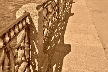 fragment of the ancient embankment with the stone sidewalk and an iron fence a closeup of color sepiaの写真素材