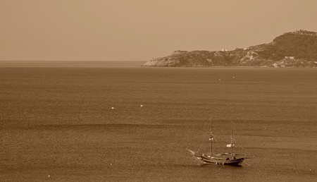 sea landscape with mountains on the horizon and one ancient yacht or the boat in the foreground in style sepia or a vintageの写真素材