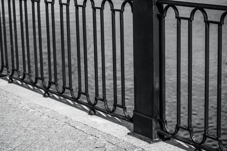 the embankment and fragment of an iron fence closeup against the background of water of monochrome toneの写真素材