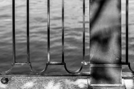 the embankment and fragment of an iron fence closeup against the background of water of monochrome toneの写真素材