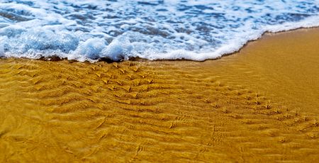 small foam wave of a surf on the sandy coastの写真素材